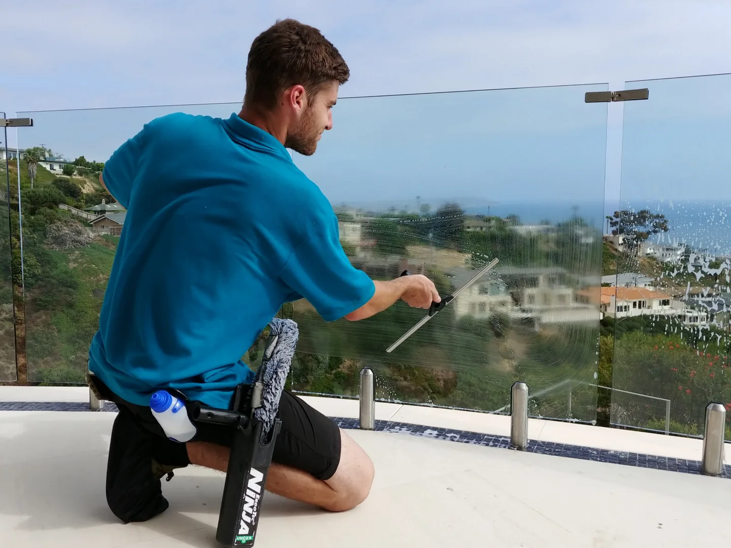 PCS technician cleaning a glass railing at a coastal home