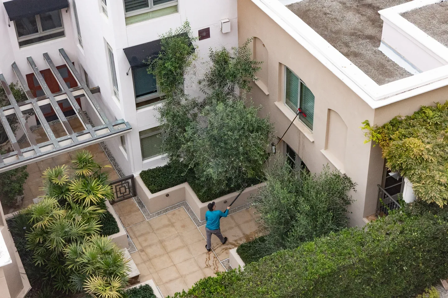 PCS technician cleaning upper courtyard windows with an extension pole at a residential community
